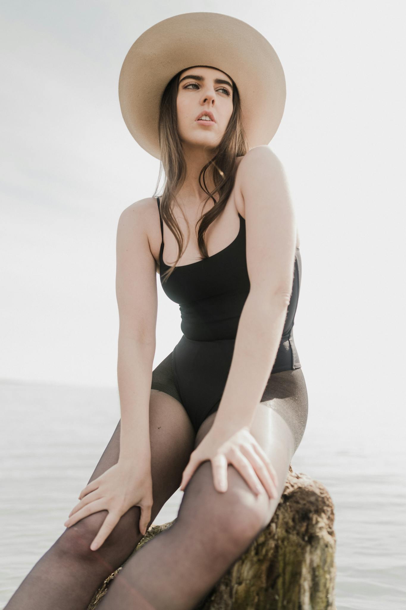 Elegant portrait of a woman in a black swimsuit and hat at the beach.